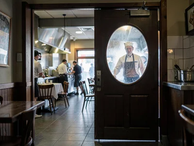 Restaurant kitchen door swinging with chef visible through round window, the fla
