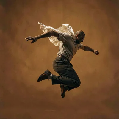 Vertical of a sky-cloaked figure mid-leap in front of a deep amber backdrop