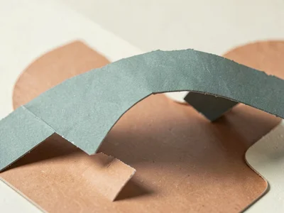 Folded paper bridge made of dusty teal cardstock arches over a small terracotta