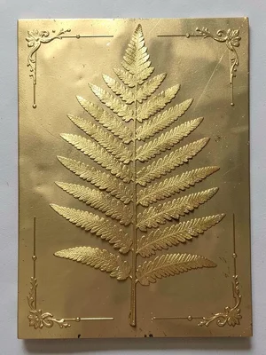 A fern frond pressed flat, gold covering the central vein and leaflet tips