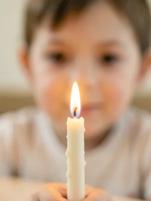 Single birthday candle in sharp focus, child's face soft and warm behind the fla