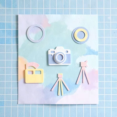 Bright cut-paper layout of camera icons (lens, flash, tripod, film) on a sky-blu