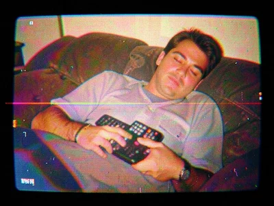 A man asleep on a couch with a TV remote on his chest, the image gently rolling