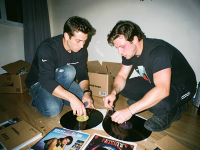 Two people dividing vinyl records on apartment floor, tension visible in body la