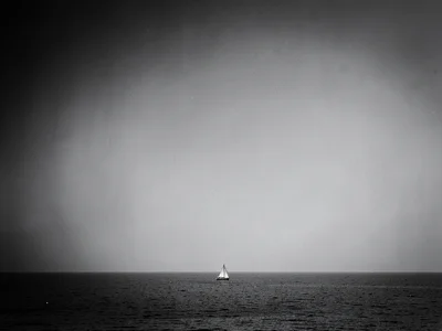 Tiny sailboat in lower third surrounded by monochrome sea and sky