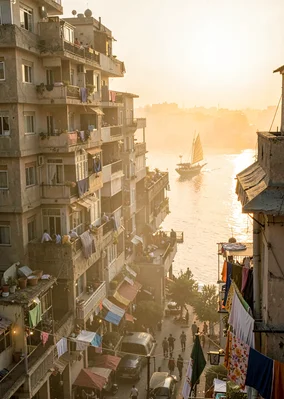 Dusty golden Cairo haze compressing apartment layers, felucca sail glimpsed betw
