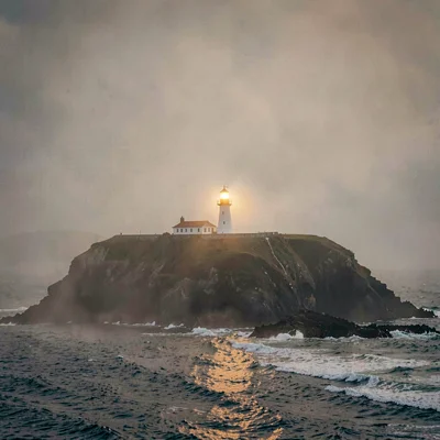 Atmospheric landscape of a fog-soaked headland with a distant lighthouse glowing