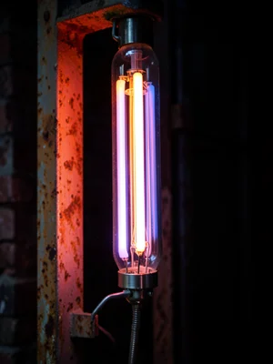 A tube mounted on a rusty metal frame, the contrast of glowing glass against cor
