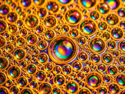 Dense oil bubble carpet on water lit from below with warm amber, honey-colored c