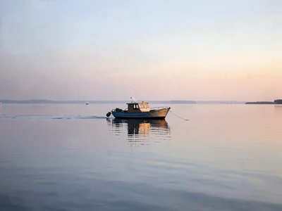 One boat on flat lake at dawn, the water and sky the same silver, floating betwe