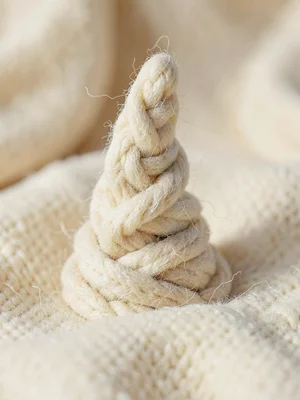 Spiraled cream knit unicorn-horn shaped from twisted cable-knit, on warm cream s