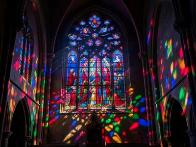 A cathedral rose window in deep blue and ruby, sunlight streaming through, casti