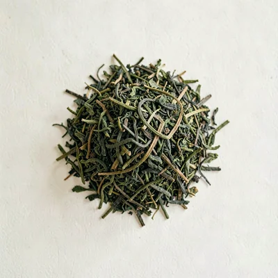 Lightbox top-down of a small mound of loose-leaf green tea on a clean cream back
