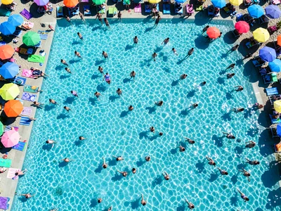 A crowded beach from above, colorful towels and umbrellas creating a mosaic, swi