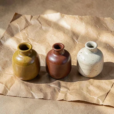 Warmstack flatlay of three ceramic vases in mustard, rust, and bone on aged kraf