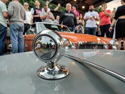 Lowrider hood ornament filling foreground, chrome distorted into funhouse mirror