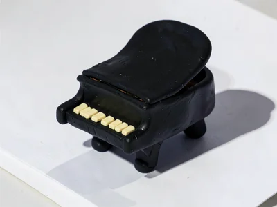 Grand chunky clay grand piano in deep black with stubby cream-toned keys and ove