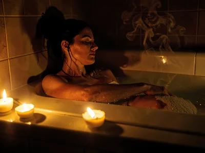Person in bath with candles on edge, the self-care flicker, steam visible in war