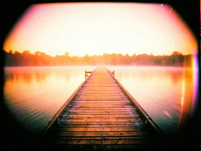 A pier stretching into a lake at dawn, the wood and water in warm amber tones, m