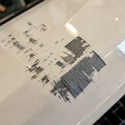 Mineral-cut macro of sandpaper scuff marks across a primered fender