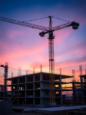 A tower crane silhouetted against a pink sunset, its lattice structure geometric