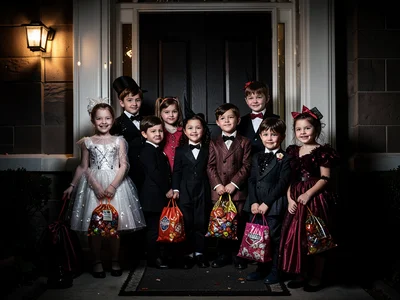 Group of costumed kids at front door trick-or-treating, porch light, candy bags