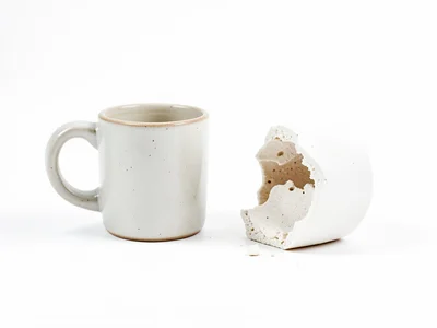 Coffee mug with handle broken off, both pieces arranged on white like archaeolog