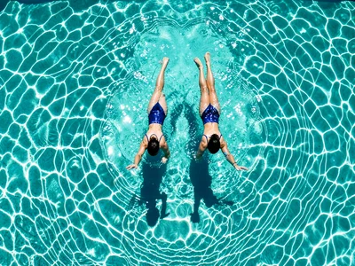 A synchronized swimming pair, their bodies creating a mirror image, the water su