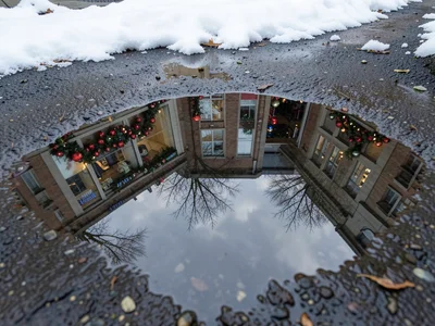 Snow-framed puddle reflecting decorated storefront, holiday shopping scene