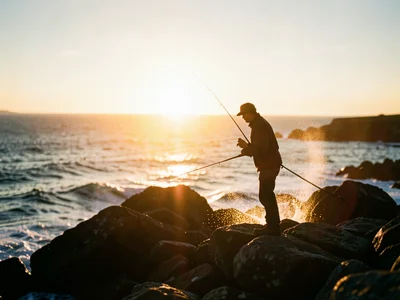 Silhouette of a lone fisherman casting from rocks on the Ring of Kerry coast, su