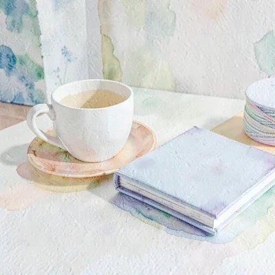 Papercraft tabletop with a paper teacup and a paper knitting book (no readable t