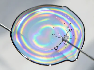 Soap bubble at the moment of popping, membrane retracting into droplet spray, ca