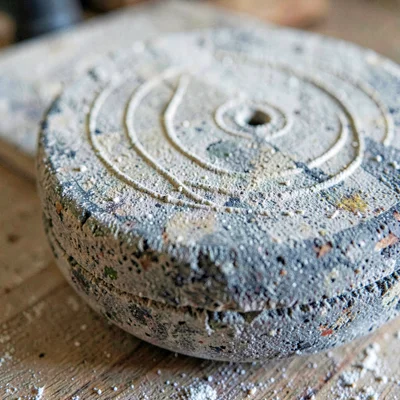 Worn-material closeup of an old grindstone face with grooves on chalky board