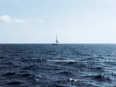 Ocean horizon where single sailboat sat still long enough to be captured