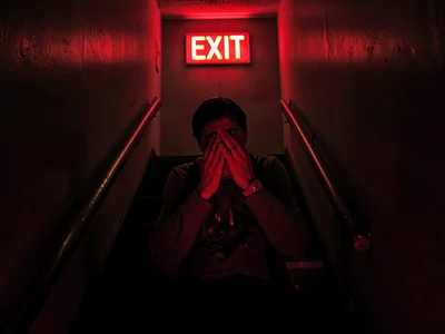 Person crying in stairwell lit only by EXIT sign, the emergency emotion in emerg