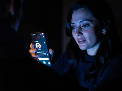 Person on dating app, swiping in dark bar, phone glow on hopeful face, the searc