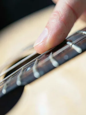 Guitarist's fingertip pressing fret, string indentation visible, neck of guitar 