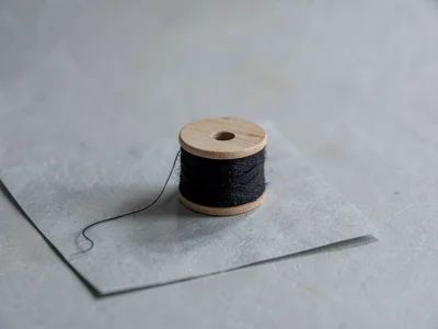 One black-stained wooden spool of unbleached cotton thread resting on cool-grey