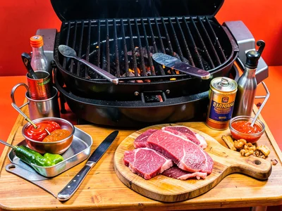 Grill setup with tools, sauces, cutting board, raw meat ready, organized