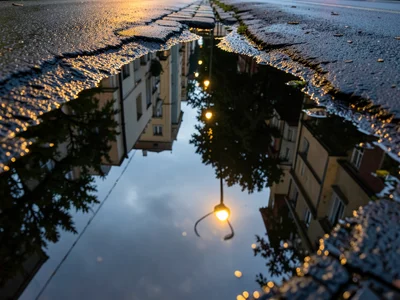 Streetlight reflecting in a chain of connected puddles along a gutter, repeated 