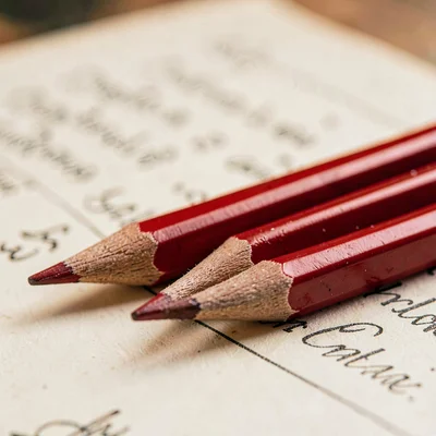 Macro of three sharpened red pencils lined up beside a manuscript