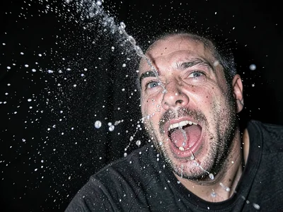 Sneeze captured at peak with visible droplet spray pattern against dark backgrou