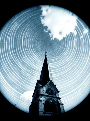 A church steeple against sky dense with overlapping arc trails