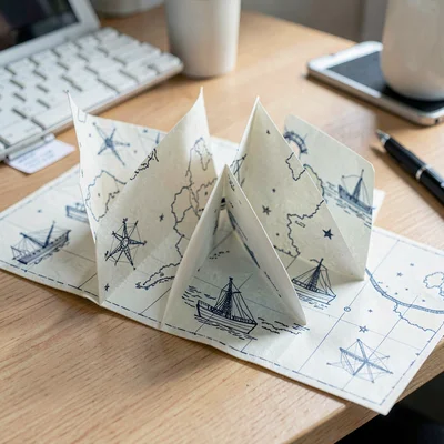 Folded paper accordion of nautical map shapes spreading across a desk, soft fibe