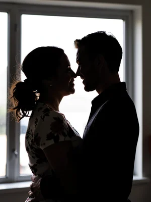 A couple in silhouette against a bright window, faces close, bodies merged