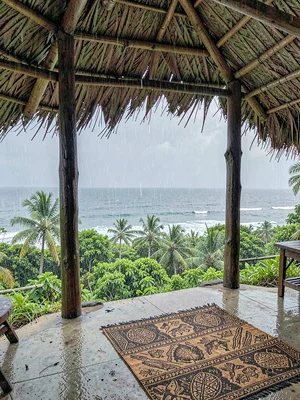 Open-air fale life in Samoa after rain, Wooden fale posts framing a view of rain