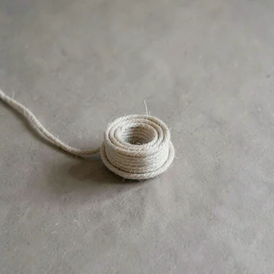 A single coil of waxed cotton cord resting on warm-grey paper, fibres faintly st