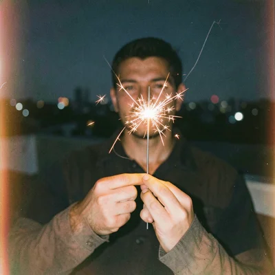 Someone's hands holding a sparkler on a rooftop at night, the spark trails long 