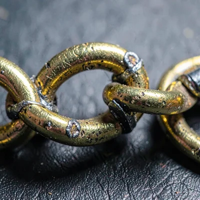 Worn-texture macro of a gold chain link with worn solder joints, sharp cold ligh