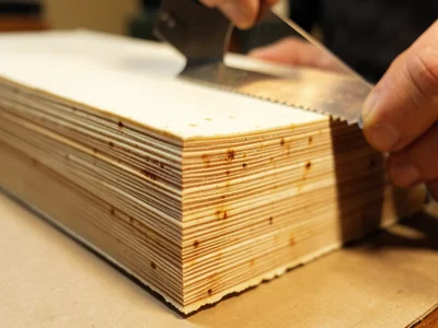 Hands trimming handmade paper with a deckle edge ruler